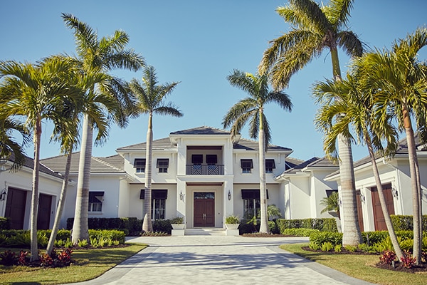 A two story Naples home with lots of palm trees and a long driveway.