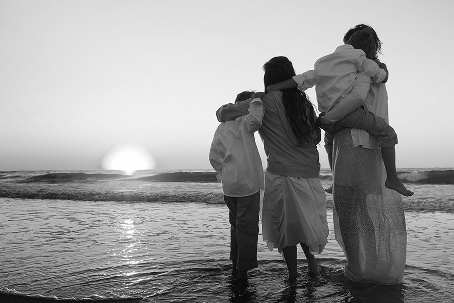 A family hugging each other while standing on the beach surrounded by the sea during the sunset