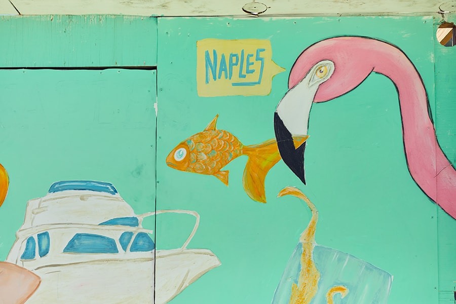 A mural of a pink flamingo holding an orange fish in its beak and a boat in the background.