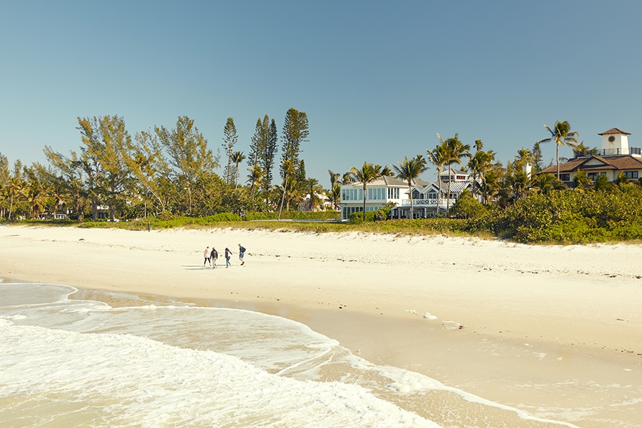 A family walking along the sandy white beaches with a luxury home in the background.