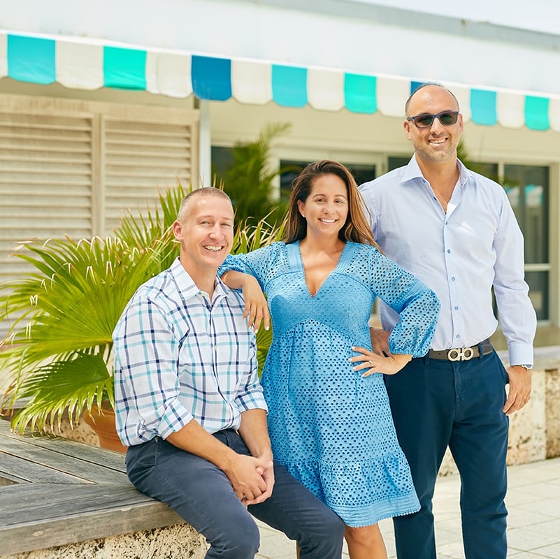 Drew Josephson sitting on the wall with his wife, Chanel Josephson leaning on his shoulder and Andrew Ventura standing next to her in front of a Naples Store