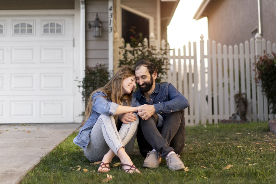 Couple sitting in front of newly bought home to start using real estate investments to diversify their portfolio
