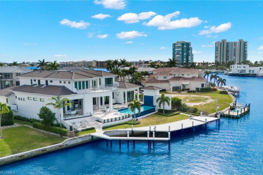 Aerial view of multi-story luxury home on canal with pool and and dock