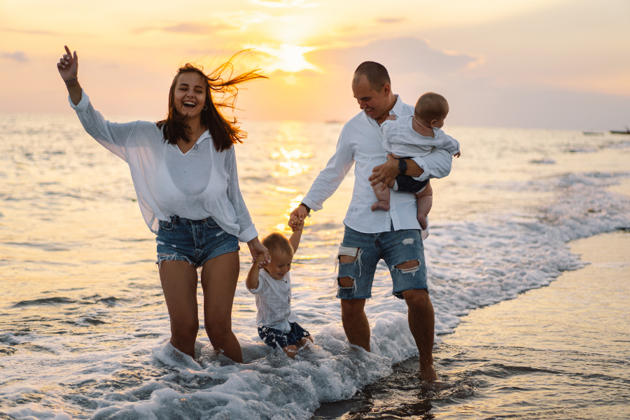 Happy young couple holding and playing with their kids in the waves on the beach at sunset